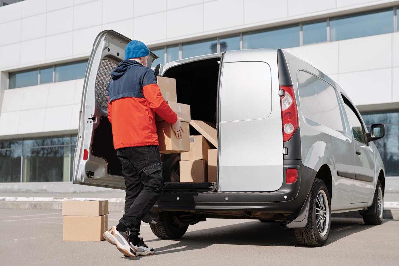 team-03 Man in colorful jacket loading cardboard boxes into a van outside an office building.